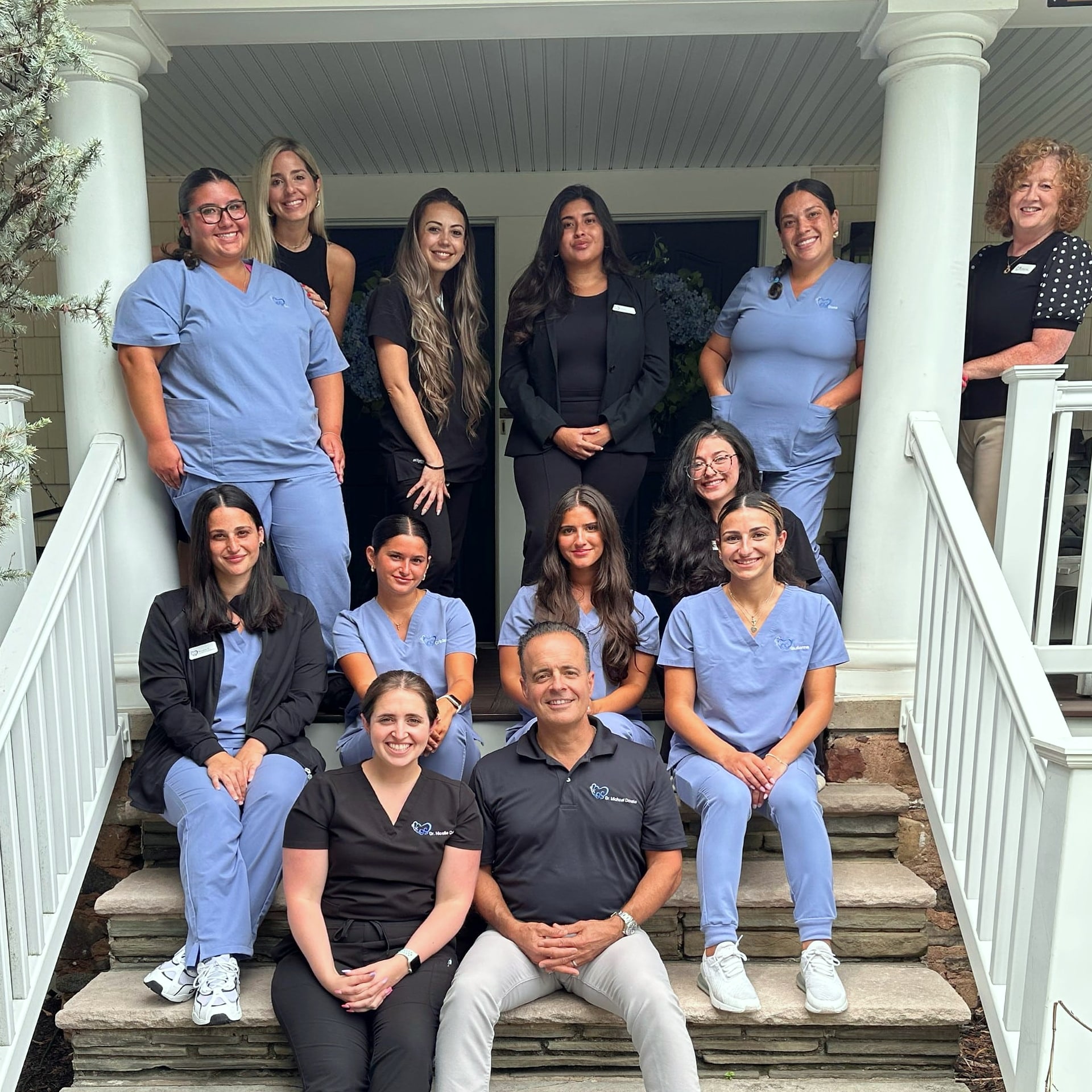 Group of twelve staff in scrubs posed on porch steps